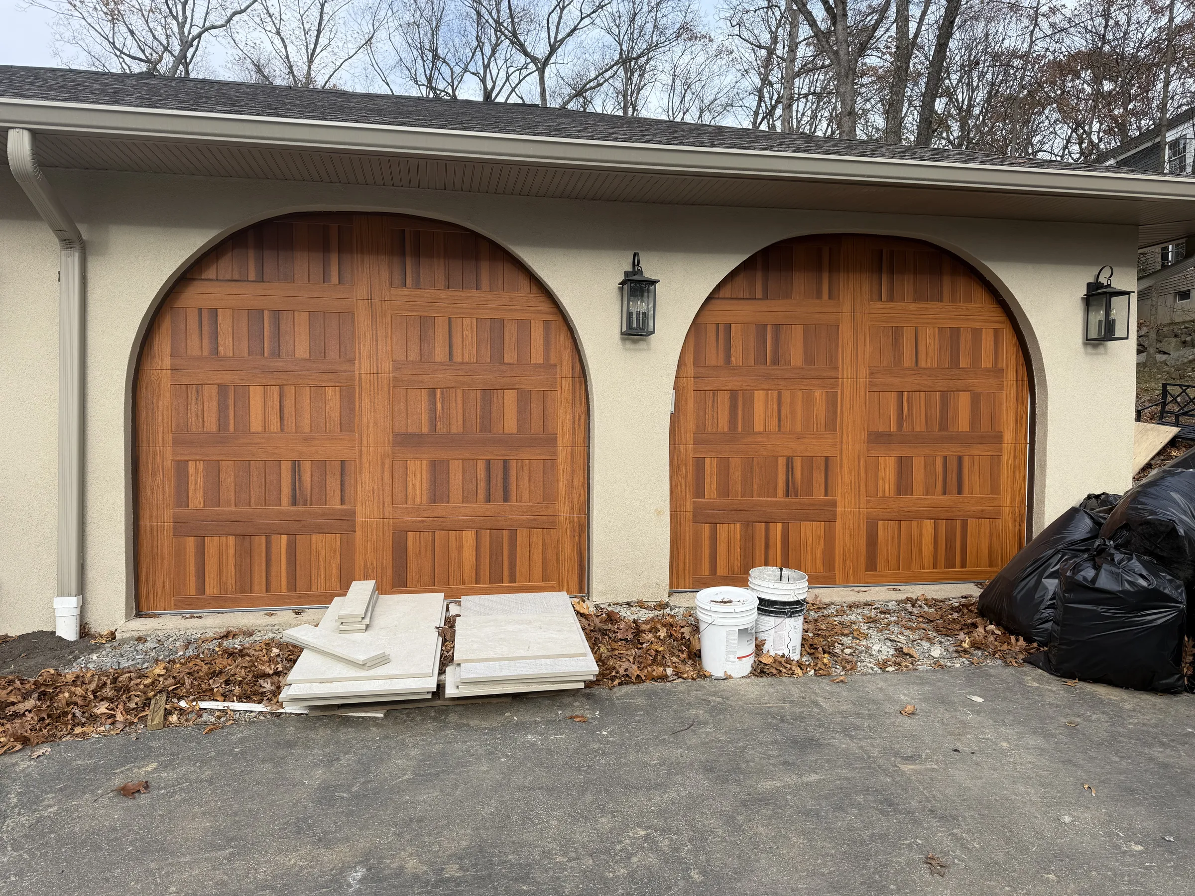 Two wood-look garage doors installed in matching arched openings on a residential home.