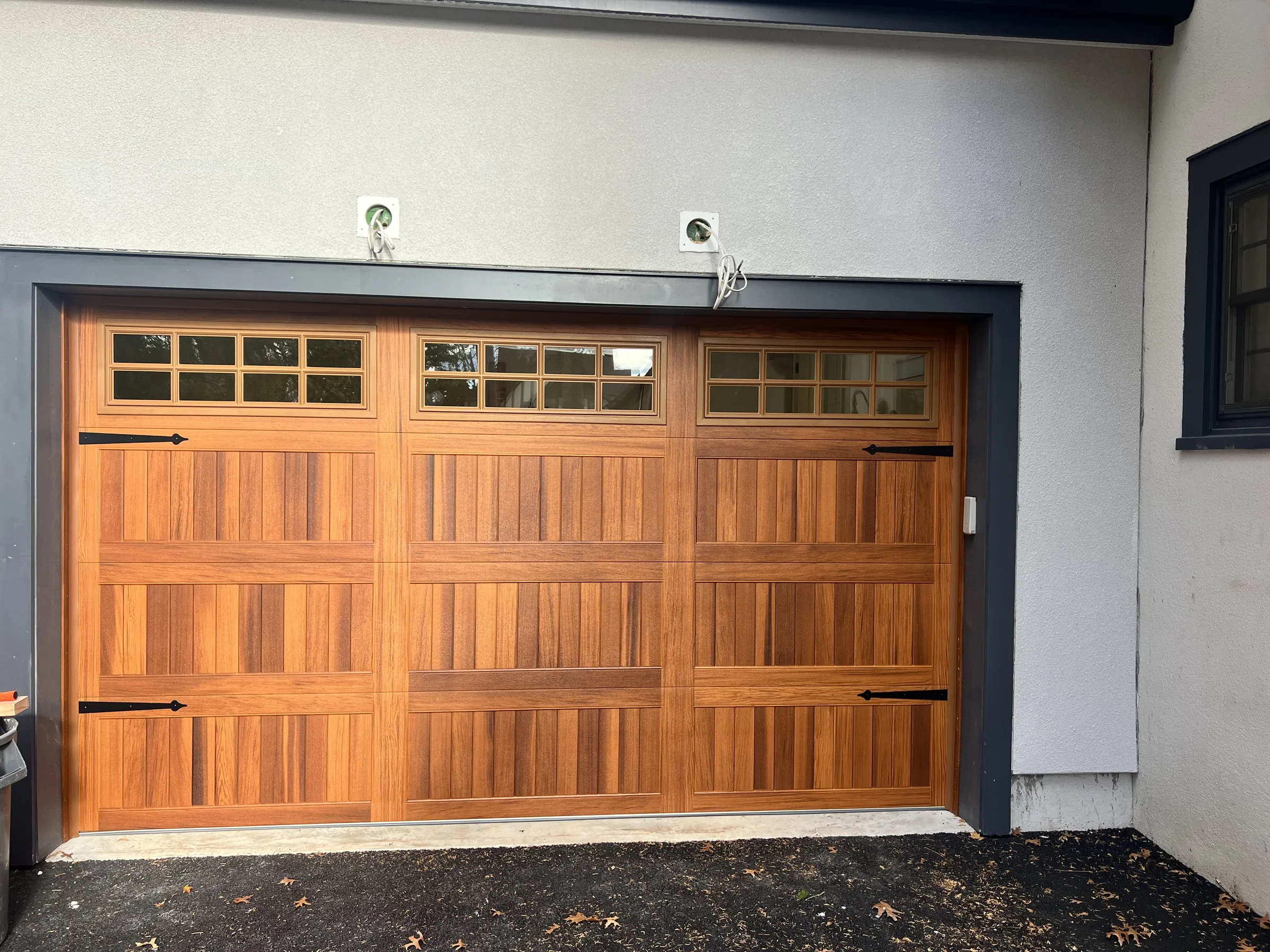 Wood-look carriage-style garage door with upper windows and black decorative hardware on a residential garage.