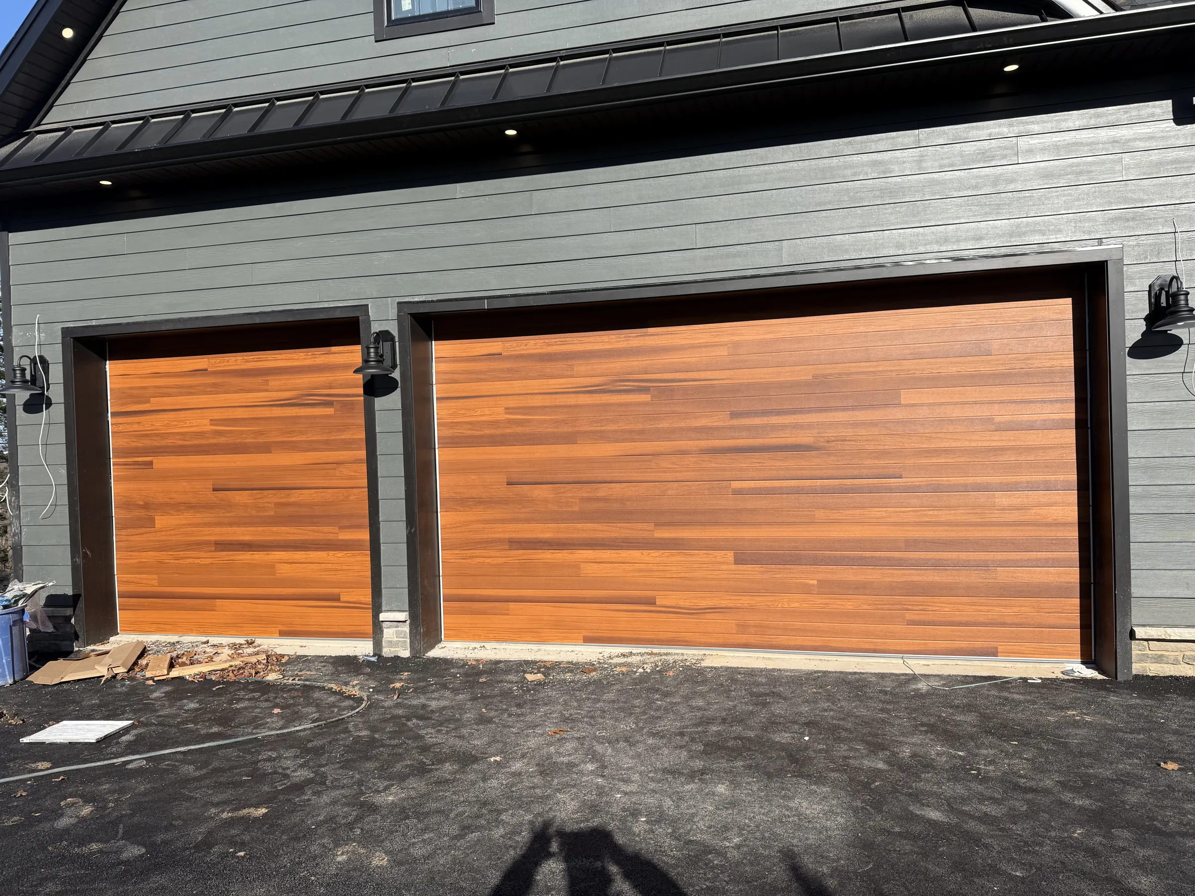 Flush wood-look single and double garage doors installed on a dark gray residential home.
